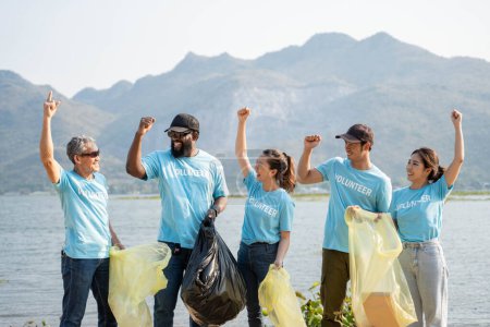 Téléchargez les photos : Heureux groupe de jeunes bénévoles qui aident à garder la nature propre et ramasser les ordures d'un rivage sablonneux. - en image libre de droit