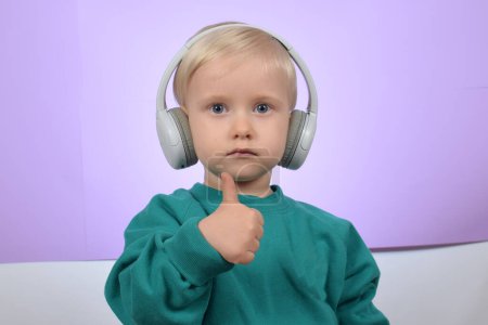 Photo for Funny boy child listens to music in headphones and shows thumbs up - Royalty Free Image