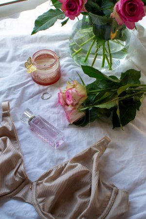 Photo for Women's bra, pink roses and perfume on a white sheet - Royalty Free Image
