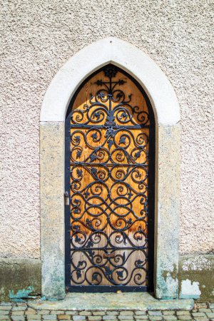 A small wooden door with a forged metal grille in the wall of the abbey.