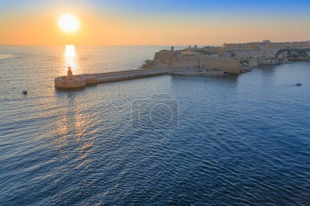 Sunrise view of the lighthouse on the Ricasoli breakwater in Valletta Grand Harbour, Malta.