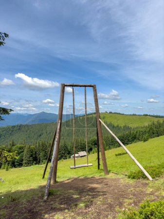 Large wooden swing with a picturesque view of the mountains on a sunny summer day. Recreation place for tourists in the mountains. Vertical photo