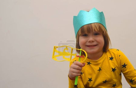 Photo for A little boy in a crown plays with a raashan. Jewish holiday Purim. Birthday, happy holidays. Isolate on white background, space for text - Royalty Free Image