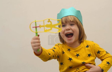 Photo for A little boy in a crown plays with a raashan. Jewish holiday Purim. Birthday, happy holidays. Isolate on white background, space for text - Royalty Free Image