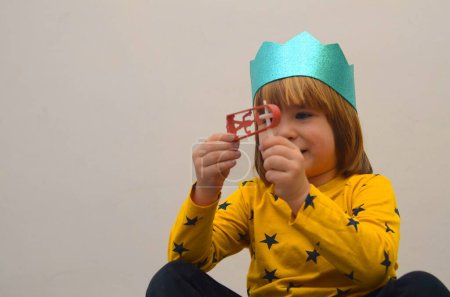 Téléchargez les photos : A little boy in a crown plays with a raashan. Jewish holiday Purim. Birthday, happy holidays. Isolate on white background, space for text - en image libre de droit
