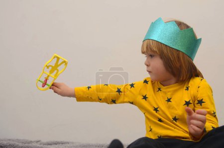 Téléchargez les photos : A little boy in a crown plays with a raashan. Jewish holiday Purim. Birthday, happy holidays. Isolate on white background, space for text - en image libre de droit