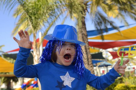 Téléchargez les photos : Carnaval, Pourim en Israël. Un petit garçon joyeux dans un chapeau, des lunettes drôles, une perruque avec un hochet, Raashan. Portrait d'un enfant en costume de Klana, des vacances drôles, un anniversaire, une mascarade. - en image libre de droit