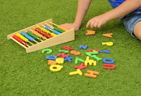 Foto de Un niño en edad preescolar juega con letras inglesas. Aprender el alfabeto en el jardín de infantes. El niño se ríe - una divertida lección sobre la hierba Copiar el espacio - Imagen libre de derechos