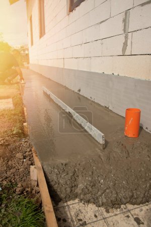 Frisch gegossener Betonestrich mit Metallgitter zur Bewehrung. Nahaufnahme. Maurer nivellieren und streichen Betonboden mit Quadratkelle vor dem Haus.