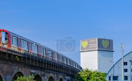 Téléchargez les photos : Londres, Angleterre - 15 juin 2023 : Un train passe à North Kensington avec la bannière Forever dans nos cœurs visible sur la tour Grenfell en arrière-plan - en image libre de droit