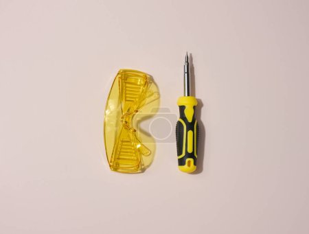 Foto de Gafas acrílicas transparentes y un destornillador sobre fondo beige, vista superior - Imagen libre de derechos