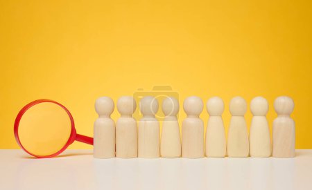 Wooden figures of men stand on a yellow background and a red plastic magnifying glass. Recruitment concept, search for talented and capable employees, career growth