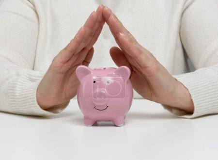 Photo for A ceramic piggy bank and female hands above it, a concept of saving money - Royalty Free Image