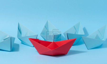 Ein rotes Papierboot steht vor einer Gruppe blauer Papierboote, eine Konfrontation