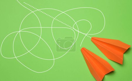 Photo for Two paper orange airplanes with different trajectories on a green background, the best solution in business - Royalty Free Image