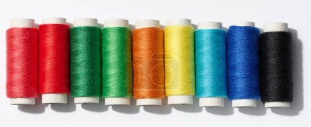 Multicolored spools of sewing threads on a white background, top view