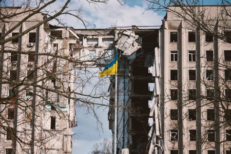 Flag of Ukraine against the background of a destroyed building in Ukraine. The building was destroyed by a Russian air bomb. Symbol of resilience and invincibility of the people of Ukraine