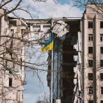 Flag of Ukraine against the background of a destroyed building in Ukraine. The building was destroyed by a Russian air bomb. Symbol of resilience and invincibility of the people of Ukraine
