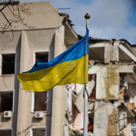 Téléchargez les photos : Drapeau de l'Ukraine dans le contexte d'un bâtiment détruit en Ukraine. Le bâtiment a été détruit par une bombe aérienne russe - en image libre de droit
