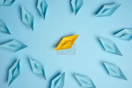 A group of blue paper boats surrounded one yellow boat, the concept of bullying, search for compromise. Top view