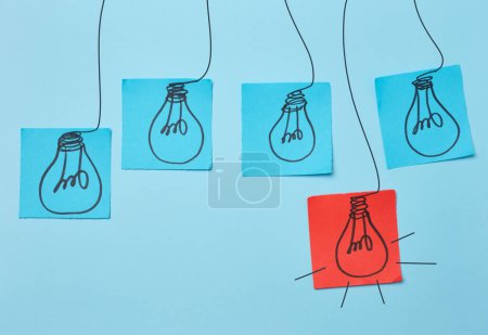 Photo for Drawn electric lightbulbs on paper sheets with a blue background, signifying the concept of searching for new ideas. - Royalty Free Image