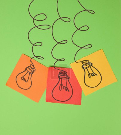 Photo for Drawn electric lightbulbs on paper sheets with a green background, signifying the concept of searching for new ideas - Royalty Free Image