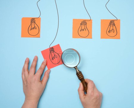 Drawn electric lamps on stickers, concept of searching for new ideas, brainstorming. Woman's hand holding a magnifying glass and a sheet of paper