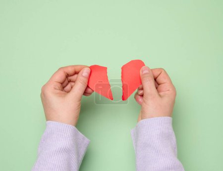 Two female hands tearing a red paper heart, symbolizing divorce or disappointment in relationships