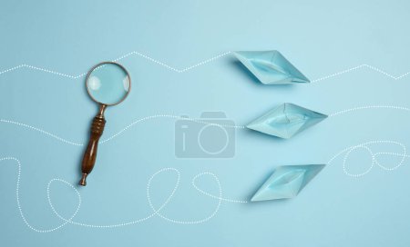 Blue paper boats and a magnifying glass, viewed from above