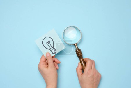 Drawn electric lamps on stickers, concept of searching for new ideas, brainstorming. Woman's hand holding a magnifying glass and a sheet of paper