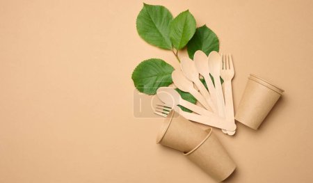 Foto de Copas de papel, cucharas de madera y tenedores sobre un fondo beige, vista superior - Imagen libre de derechos