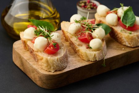 Foto de Mozzarella redonda, tomates cherry y microgreens en un pedazo de pan blanco, mesa negra - Imagen libre de derechos