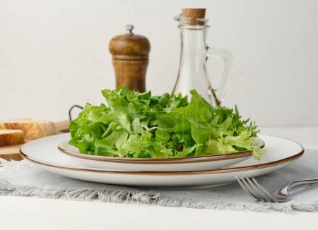 Foto de Hojas de lechuga verde fresca en un plato blanco sobre la mesa, comida saludable - Imagen libre de derechos