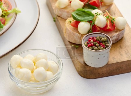 Foto de Bolas de mozzarella en tazón de vidrio y ensalada sobre un fondo blanco, de cerca - Imagen libre de derechos