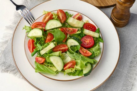 Foto de Ensalada de tomates cherry picados y pepinos en un plato redondo blanco sobre la mesa, comida saludable. Vista superior - Imagen libre de derechos
