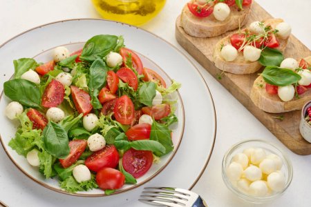 Foto de Ensalada con mozzarella, tomates cherry y lechuga verde en un plato redondo blanco sobre la mesa, vista superior - Imagen libre de derechos