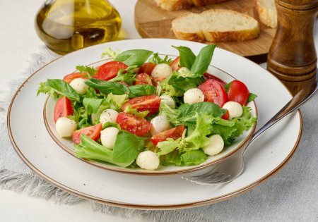 Foto de Ensalada con mozzarella, tomates cherry y lechuga verde en un plato redondo blanco sobre la mesa - Imagen libre de derechos