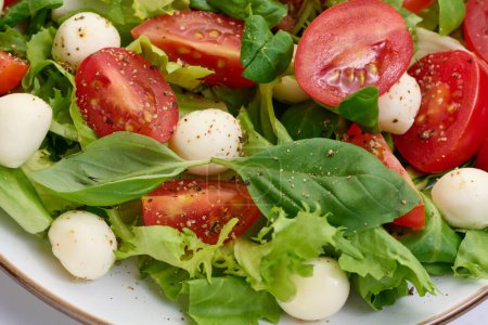 Foto de Ensalada con mozzarella, tomates cherry y lechuga verde en un plato redondo blanco, primer plano - Imagen libre de derechos