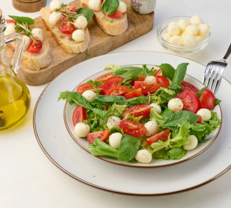 Foto de Ensalada con mozzarella, tomates cherry y lechuga verde en un plato redondo blanco sobre la mesa, cerrar - Imagen libre de derechos