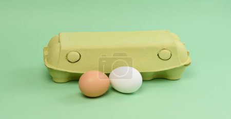 Foto de Dos huevos de pollo en una caja de papel sobre un fondo verde, de cerca - Imagen libre de derechos