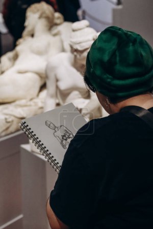 Foto de Florencia, Italia - 29 de diciembre de 2023: Un joven artista está pintando en la Galería de la Academia de Florencia, un museo de arte en Florencia, Italia. - Imagen libre de derechos