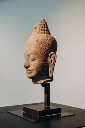 Foto de Niza, Francia - 19 de noviembre de 2023: Cabeza de una deidad budista femenina. Desde Camboya, finales del siglo XII, estilo Bayon, piedra arenisca gris - Imagen libre de derechos