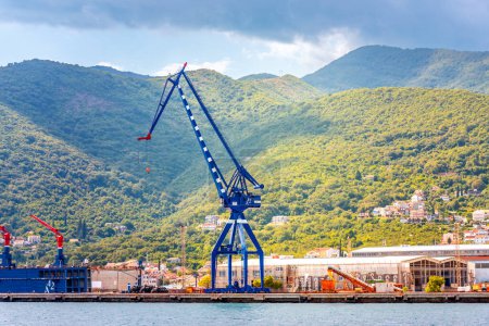 Foto de Kotor, Montenegro - 10 de agosto de 2023: Grúa portuaria en la orilla del mar Adriático con el telón de fondo de montañas. Montenegro, Bahía de Kotor - Imagen libre de derechos
