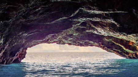 Foto de Cueva con apertura al mar azul con nubes en el horizonte. - Imagen libre de derechos