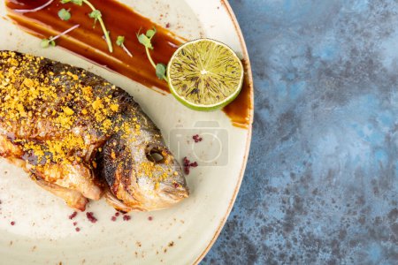 délicieux dorado grillé ou poisson de daurade avec citron vert, microgreens et sauce sur plateau blanc sur table bleue