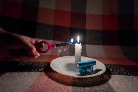 Eine Frau zündet mit einem Gasfeuerzeug eine Kerze an. In der Nähe der Kerze befinden sich drei entladene zylindrische Batterien (Nahaufnahme). Stromausfall-Konzept. Stromausfall. Energiekrise