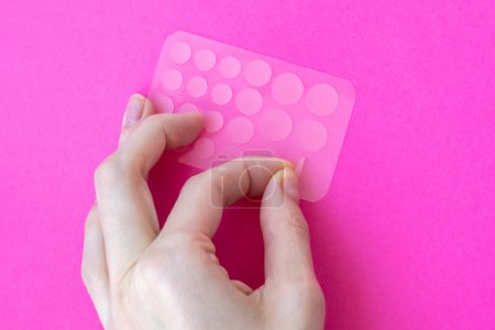 Photo for Woman tears off an acne patch to stick on her skin. Acne patches on a pink background View from above - Royalty Free Image