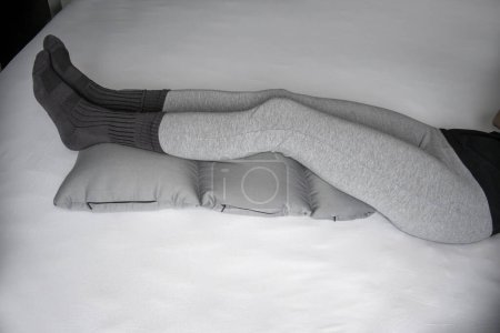 Foto de Las piernas de las mujeres se encuentran en un cojín especial para las piernas para la relajación y la prevención de las venas varicosas. - Imagen libre de derechos