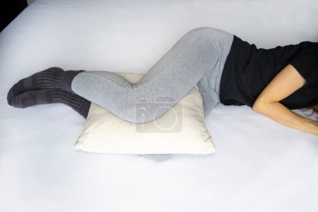 Foto de Leg cushion for sleeping for knee pain. Orthopedic pillow between the legs of a lying woman in pajamas. - Imagen libre de derechos