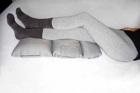 Foto de Mujer delgada descansa con las piernas en una almohada ortopédica para la salud de las venas y la mejora de la circulación - Imagen libre de derechos